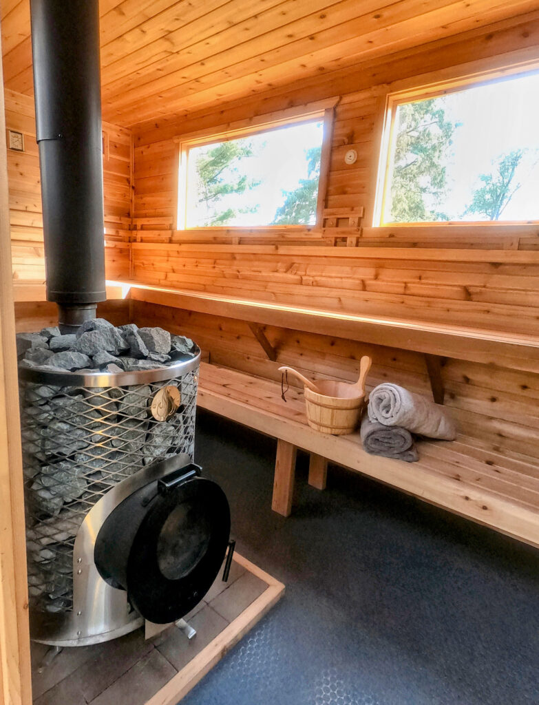 Interior of the mobile sauna glowing in the natural light provided by the sauna's three large windows. Cedar paneling walls, ceiling, and benches provide the perfect atmosphere for your relaxing wood fired sauna experience.